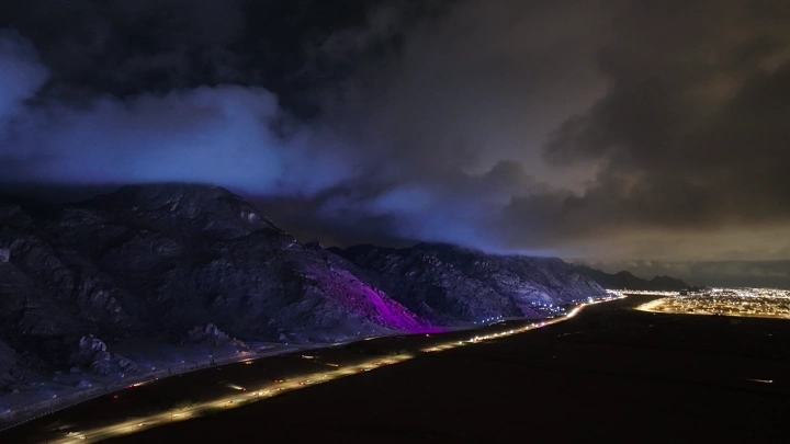 جبال مضاءة في حائل ليلاً تحت سماء غائمة، منظر جوي.