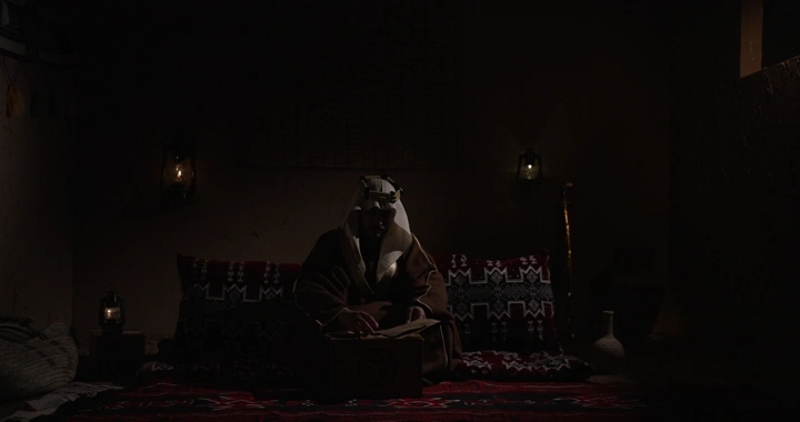 رجل سعودي يكتب في غرفة تقليدية، إضاءة خافتة.