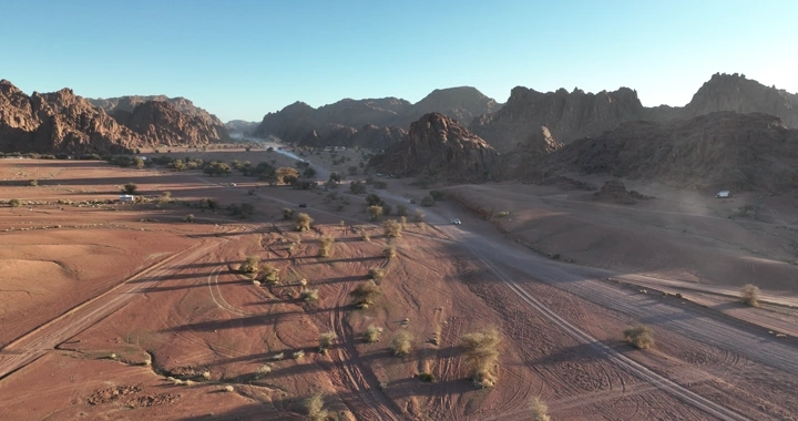 منظر جوي لصحراء وجبال مع آثار سيارات دفع رباعي، في النهار.