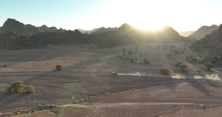 جيب شاص يسير في وادي صحراوي عند الغروب، لقطة جوية.