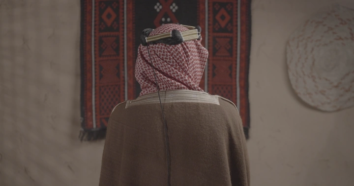 رجل سعودي بالزي يوم التاسيس أمام سجادة حائط، لقطة داخلية.