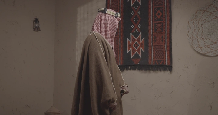 رجل سعودي يرتدي الزي التقليدي في غرفة مزينة بسجادة، لقطة جانبية.