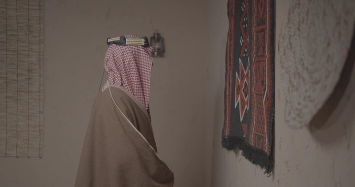 رجل يرتدي الزي السعودي التقليدي يلمس سدو على الحائط، لقطة داخلية.