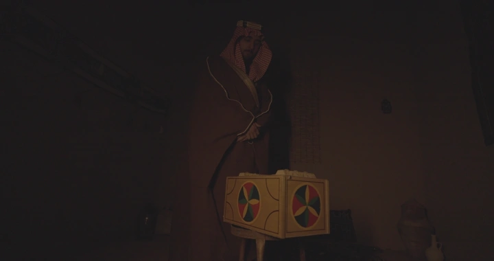 رجل سعودي يفتح صندوقًا في غرفة مظلمة، لقطة داخلية.