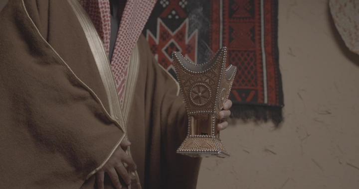رجل سعودي يحمل مبخرة تقليدية في غرفة مزينة، لقطة قريبة.