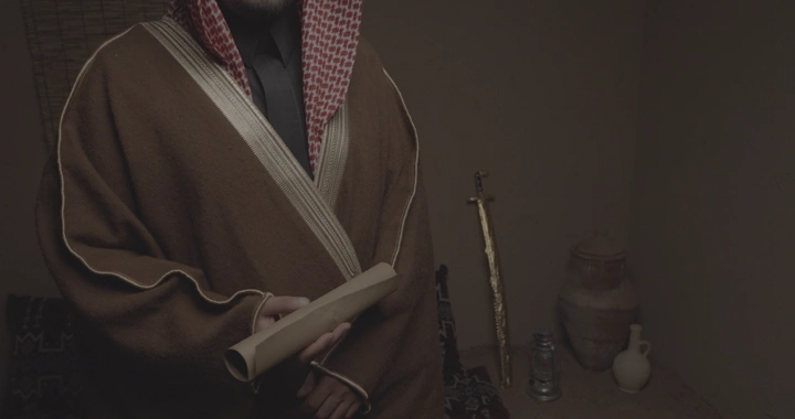 رجل يرتدي عباءة يحمل ورقة في غرفة تقليدية، لقطة داخلية.