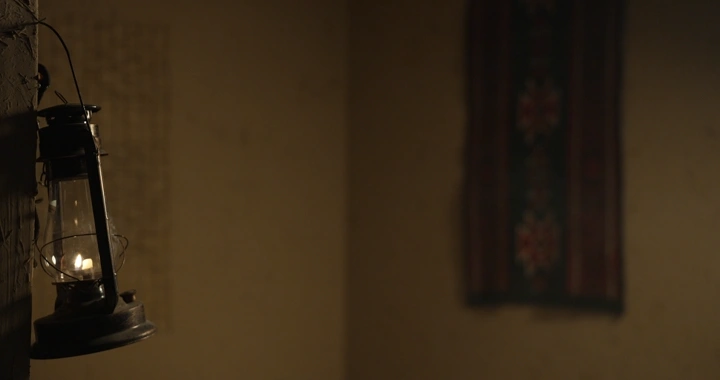 مصباح قديم معلق على جدار في غرفة تقليدية، إضاءة خافتة.