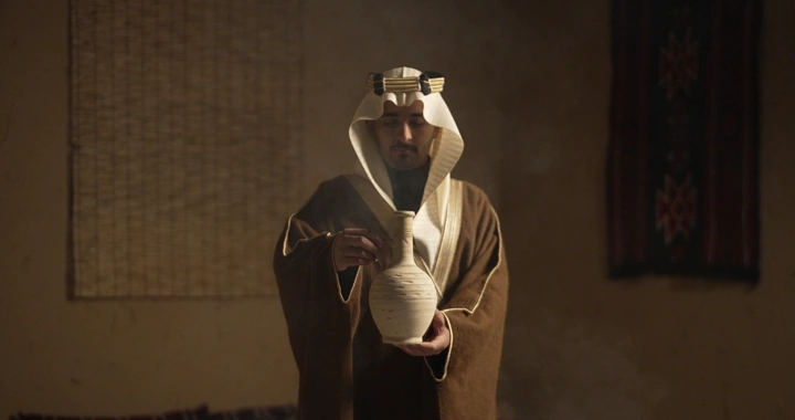 رجل سعودي يرتدي الزي التقليدي يحمل فخارًا في غرفة تقليدية، لقطة داخلية.