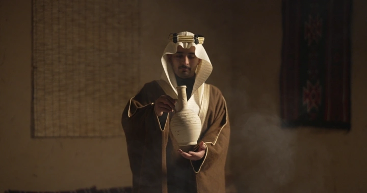 رجل سعودي يحمل فخارًا في غرفة تقليدية، إضاءة دافئة.