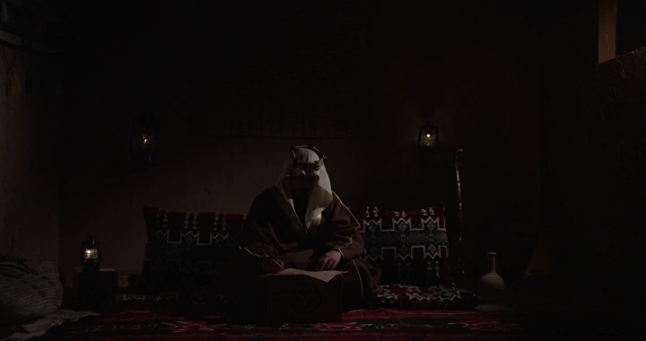 رجل سعودي يكتب في غرفة تقليدية، إضاءة خافتة.