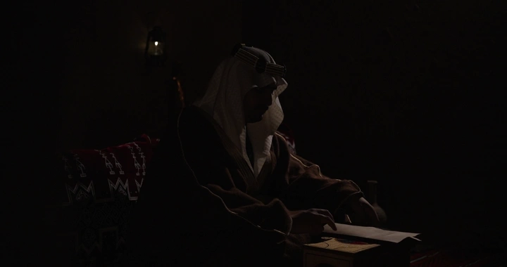 رجل سعودي يقرأ في غرفة مظلمة، إضاءة خافتة.