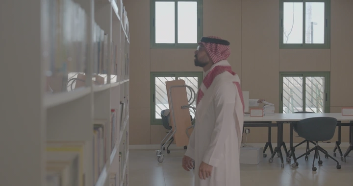 رجل يختار كتابًا من مكتبة حديثة، لقطة داخلية.