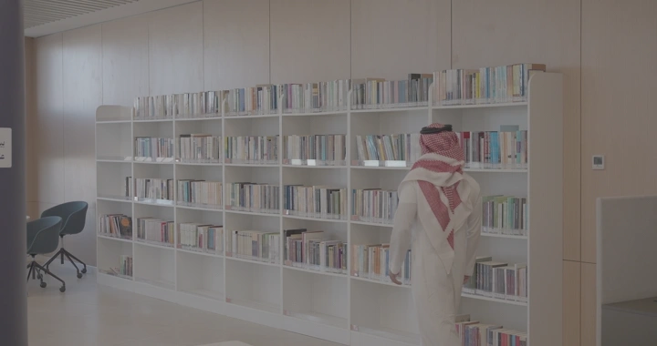 رجل يرتدي الزي التقليدي في مكتبة حديثة، لقطة داخلية.