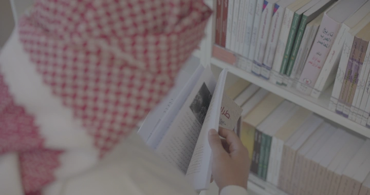 شخص يقرأ كتابًا في مكتبة، لقطة من الخلف.