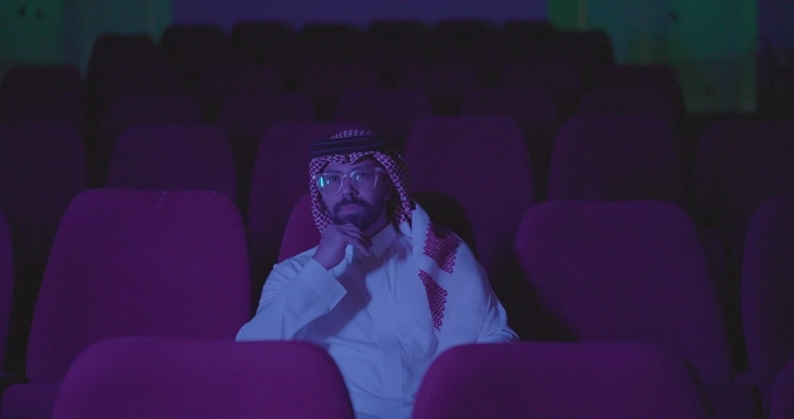 رجل يجلس في سينما فارغة، إضاءة خافتة، لقطة أمامية.
