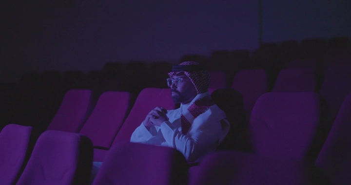 شخص يجلس في سينما مظلمة، إضاءة خافتة، لقطة داخلية.