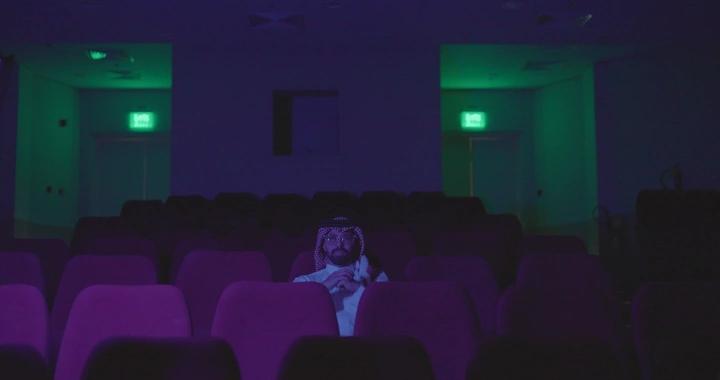 شخص يجلس في سينما مظلمة، إضاءة خافتة، لقطة داخلية.