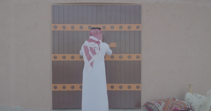 رجل يرتدي الزي التقليدي يفتح بوابة خشبية، لقطة خلفية.