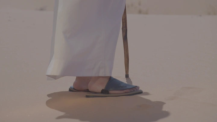 رجل يمشي على رمال الصحراء بعصا، لقطة قريبة.