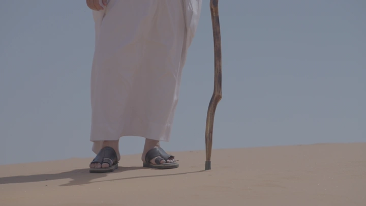 رجل يرتدي ثوبًا يمشي على رمال الصحراء، لقطة قريبة.