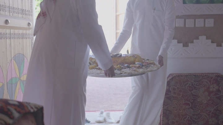 شخصان يحملان طبق مفطح في غرفة تقليدية، لقطة داخلية.