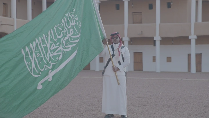 رجل يحمل العلم السعودي في قصر القشلة، لقطة نهارية.