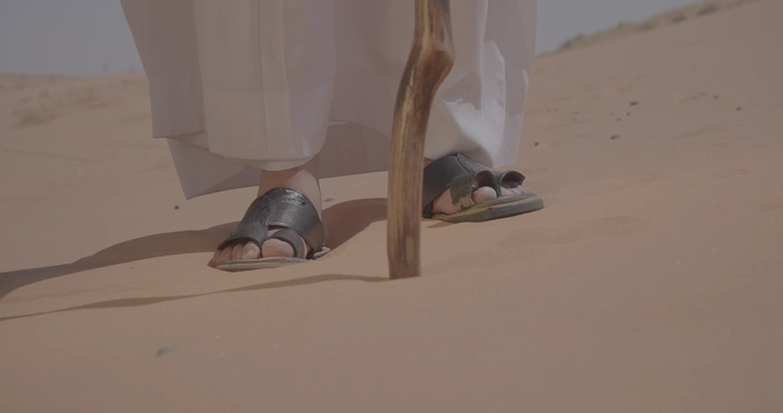 رجل يمشي في صحراء النفود بعصا، لقطة قريبة.