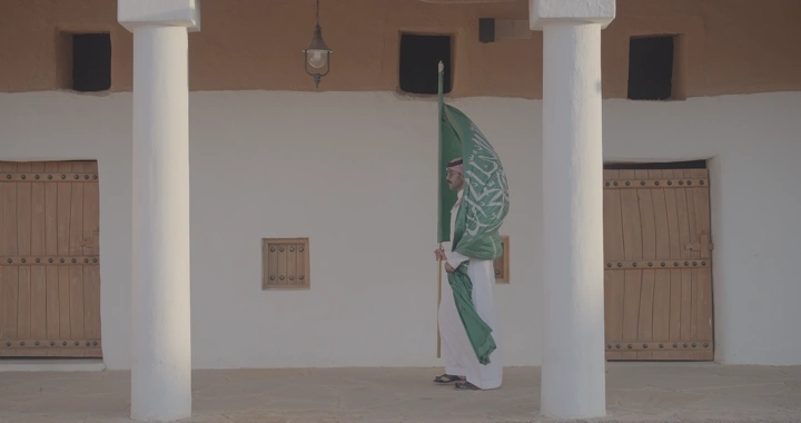 رجل يحمل العلم السعودي في قصر القشلة بحائل، لقطة جانبية.