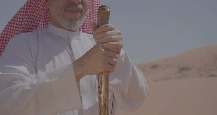 رجل يضرب العصا في النفود و يرتدي الزي التقليدي في صحراء النفود، لقطة قريبة.