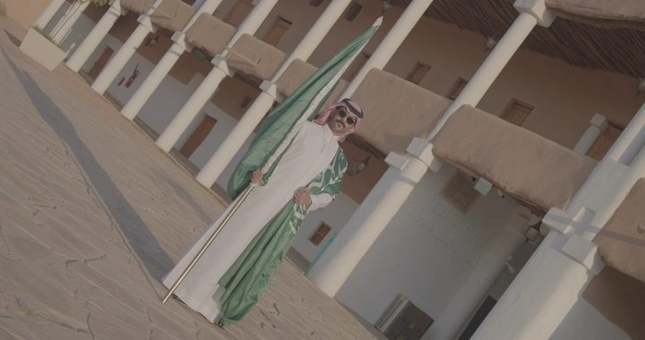 رجل يحمل العلم السعودي في قصر القشلة بحائل، لقطة واسعة.