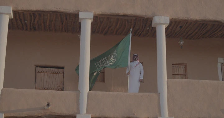 رجل يحمل العلم السعودي في قصر القشلة بحائل، لقطة أمامية.