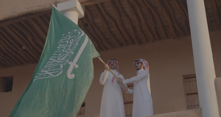 رجلان يحملان العلم السعودي في قصر القشلة بحائل، لقطة نهارية.