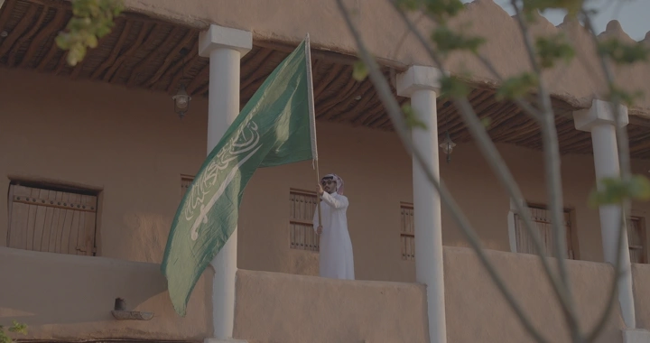 رجل يحمل العلم السعودي في قصر القشلة بحائل، لقطة من الأسفل.