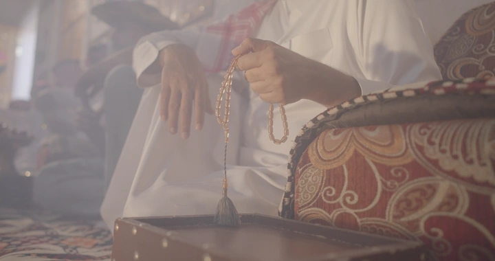 رجل يحمل سبحة في مجلس عربي تقليدي، لقطة داخلية.