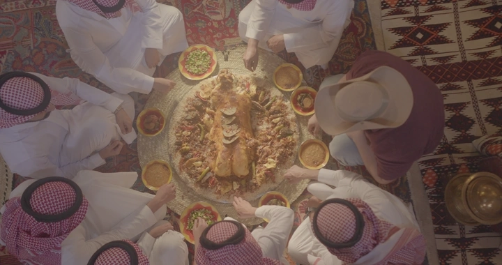 وليمة غدا مفطح تقليدية على الأرض مع أشخاص يرتدون الزي السعودي ، لقطة من الأعلى.