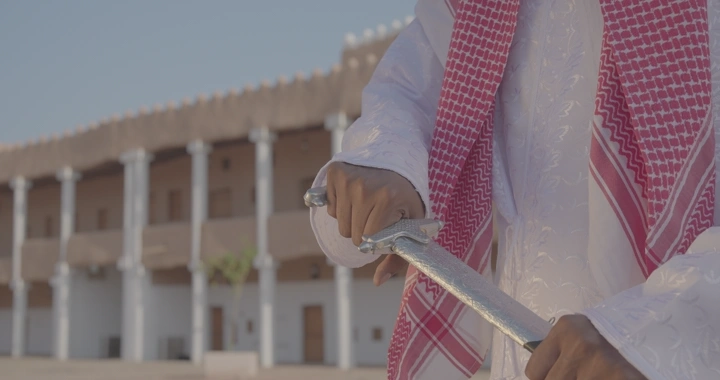 رجل يرتدي الزي التقليدي يستل السيف أمام مبنى تاريخي، لقطة قريبة.