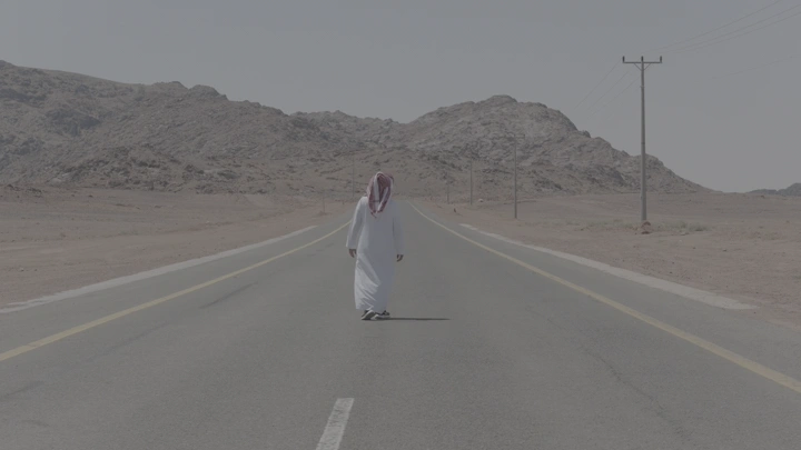 رجل يوقف سيارة لاكرامه ويرتدي ثوباً في طريق صحراوي، لقطة بعيدة.