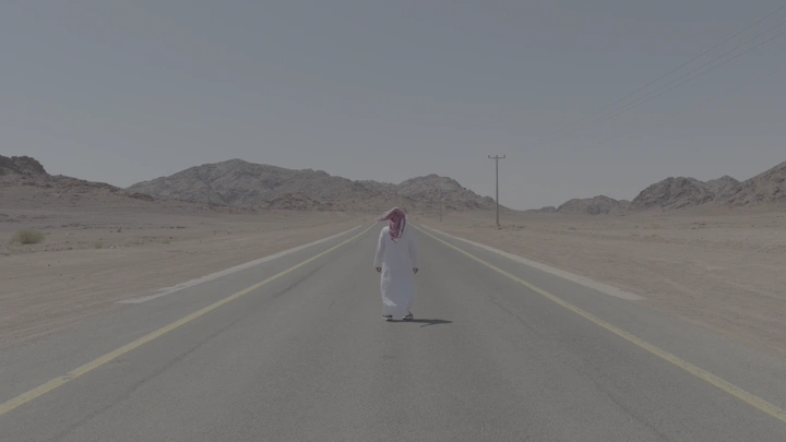 رجل يوقف سيارة لاكرامه و يرتدي ثوبًا يمشي في طريق صحراوي، لقطة نهارية.