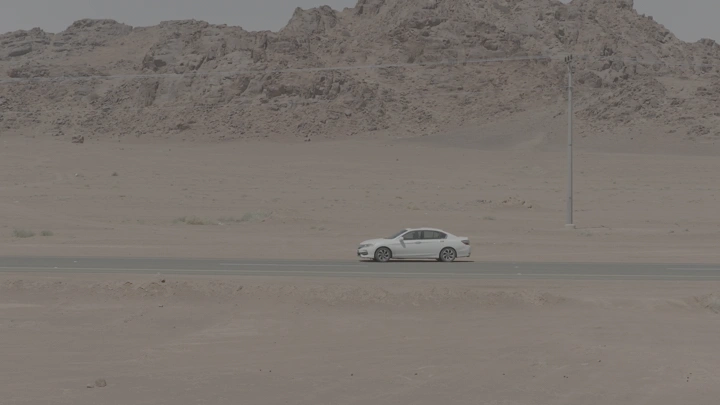 سيارة بيضاء على طريق صحراوي بجانب جبل، لقطة جانبية.