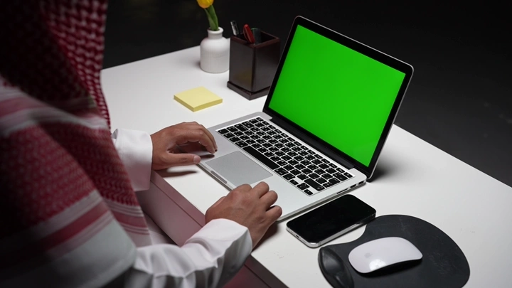 رجل سعودي يعمل على لابتوب في مكتب مع وجود شاشة خضراء كروما، لقطة مقربة.