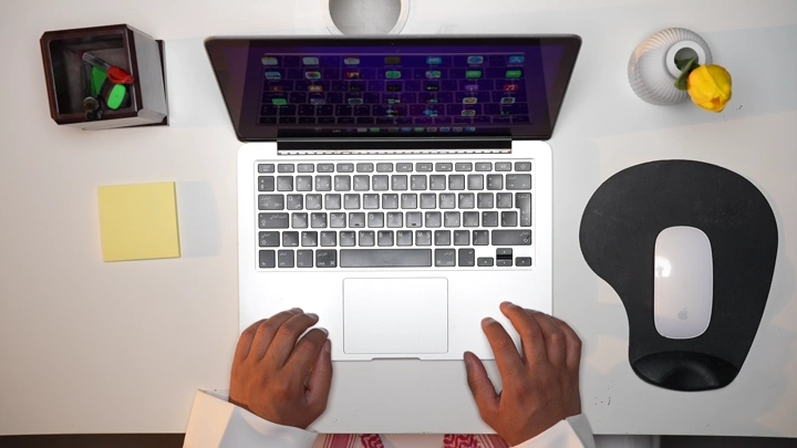 رجل سعودي يعمل على لابتوب في مكتب حديث ويسجل ملاحظاته، لقطة من الأعلى.