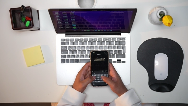 رجل سعودي يعمل داخل مكتب ويرسل رساله، لقطة من الأعلى.