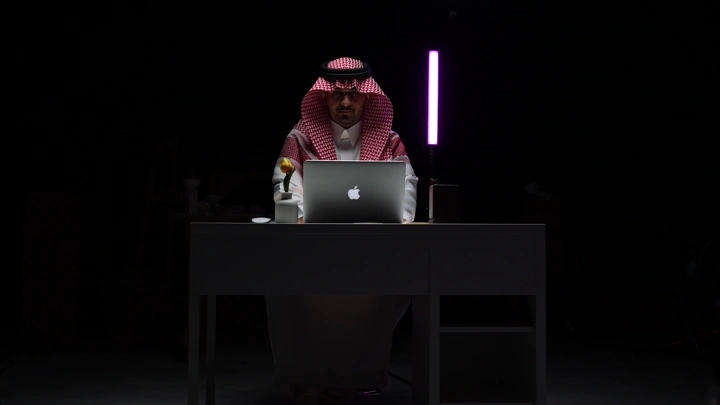 رجل سعودي يعمل على لابتوب في مكتب مظلم، لقطة أمامية.