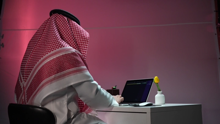 رجل سعودي يعمل على لابتوب في مكتب حديث، لقطة جانبية.
