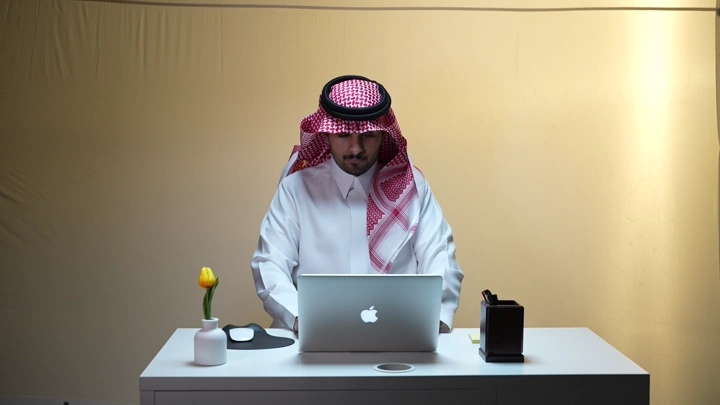 رجل سعودي يعمل على لابتوب في مكتب، لقطة أمامية.