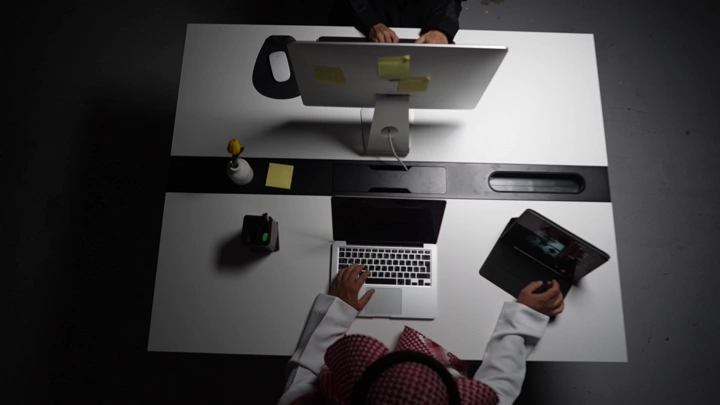 رجل سعودي يعمل على لابتوب في مكتب داخلي، لقطة علوية.
