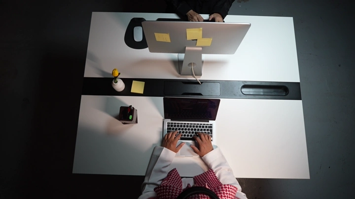 رجل سعودي يعمل على لابتوب في مكتب حديث، لقطة علوية.