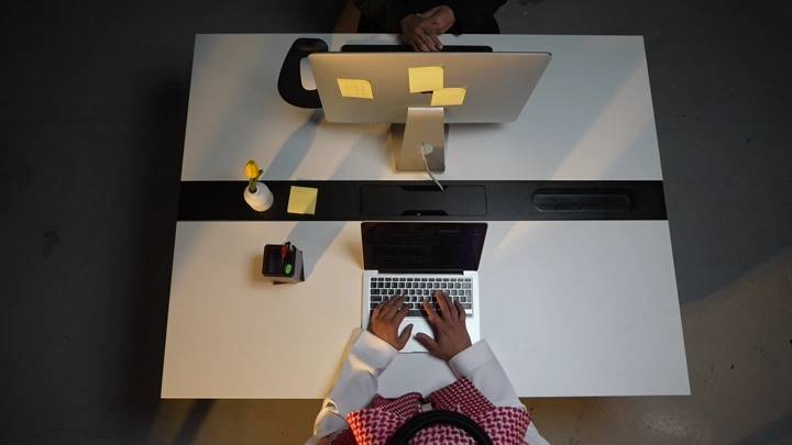 رجل سعودي يعمل على لابتوب في مكتب ، لقطة علوية.