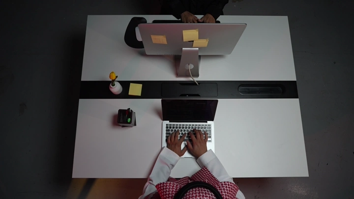رجل سعودي يعمل على لابتوب في مكتب حديث، لقطة علوية.