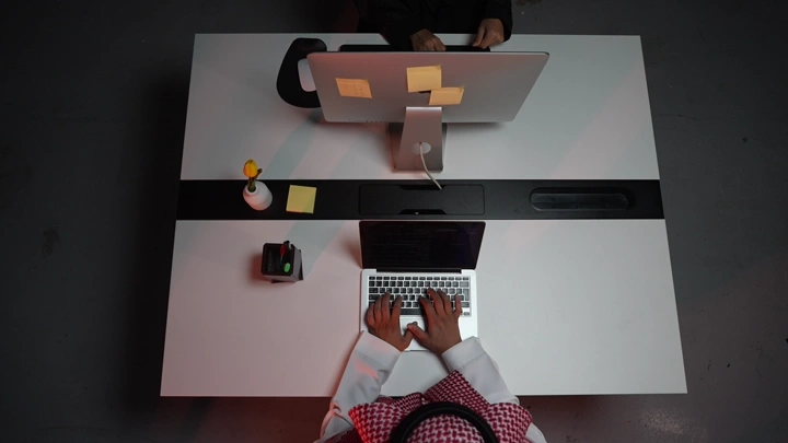 رجل سعودي يعمل على لابتوب في مكتب حديث، لقطة علوية.
